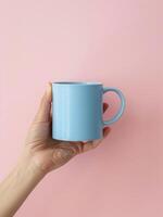 Hand Holding Blue Coffee Mug on Pink Background photo