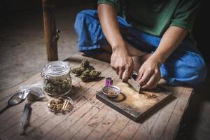 un hombre prepara marijuana en un corte tablero a fumar, persona quien fuma drogas, fármaco adicto, drogas adiccion y retirada síntomas concepto. drogasinternacional día en contra fármaco abuso. foto