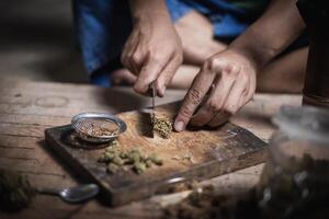 A man prepares marijuana on a cutting board to smoke, person who smokes drugs, drug addict, Drugs addiction and withdrawal symptoms concept. drugsInternational Day against Drug Abuse. photo