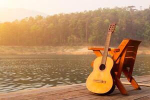 The wooden guitar was set up beside a chair on a wooden balcony in the morning over a reservoir with beautiful views of nature and bright sunshine in preparation for the upcoming party. photo