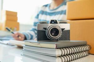 A vintage film camera sits on a table in an office and a book stands out in the background. A vintage film camera with a simple design sits on a table in an office and has copy space for text. photo