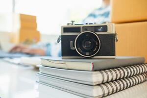 A vintage film camera sits on a table in an office and a book stands out in the background. A vintage film camera with a simple design sits on a table in an office and has copy space for text. photo