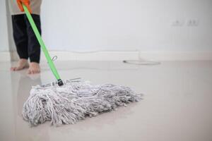 A young woman holds a mop to clean the floor and mixes disinfectant into the mop to prevent germs and bacteria. The idea of hiring a professional housekeeper to do housework and clean the house. photo
