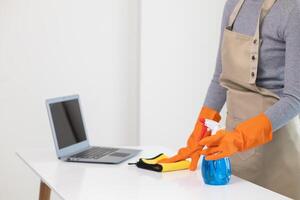 young woman puts on an apron and rubber gloves before holding spray bottle filled with cleaner and disinfectant to use to clean furniture surfaces clean and germ free. Concept of contract Hire cleaner photo