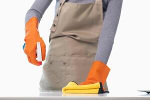 young woman puts on an apron and rubber gloves before holding spray bottle filled with cleaner and disinfectant to use to clean furniture surfaces clean and germ free. Concept of contract Hire cleaner photo