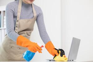 young woman puts on an apron and rubber gloves before holding spray bottle filled with cleaner and disinfectant to use to clean furniture surfaces clean and germ free. Concept of contract Hire cleaner photo