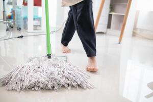 A young woman holds a mop to clean the floor and mixes disinfectant into the mop to prevent germs and bacteria. The idea of hiring a professional housekeeper to do housework and clean the house. photo
