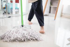 un joven mujer sostiene un fregona a limpiar el piso y mezclas desinfectante dentro el fregona a evitar gérmenes y bacterias el idea de contratación un profesional ama de casa a hacer tareas del hogar y limpiar el casa. foto