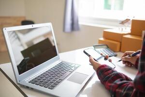 businessman decides invest in small SME business at home by using laptop and smartphone do online marketing and sell things online through an application before packing products according to orders. photo