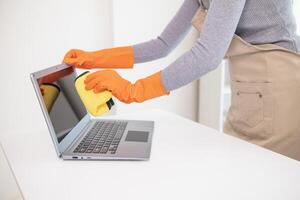 young woman puts on an apron and rubber gloves before holding spray bottle filled with cleaner and disinfectant to use to clean furniture surfaces clean and germ free. Concept of contract Hire cleaner photo