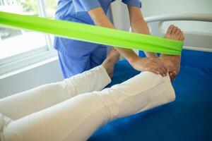 female doctor using elastic bands help patient regain muscle movement after recuperating from muscle injury and wants rehabilitate her be able use her normal daily life by practicing physical therapy photo