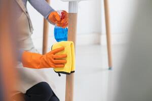 young woman puts on an apron and rubber gloves before holding spray bottle filled with cleaner and disinfectant to use to clean furniture surfaces clean and germ free. Concept of contract Hire cleaner photo