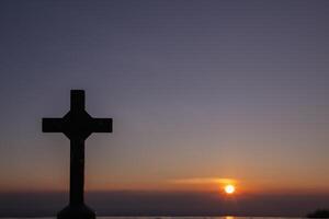 The silhouette of a cross on the background of a twilight sunset is a symbol of God and the cross is also believed to be of His divinity. The cross is a symbol of God loving kindness for all people. photo