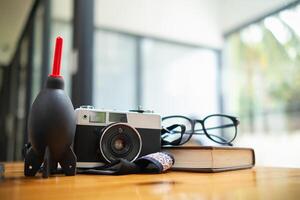 A vintage film camera sits on a table in an office and a book stands out in the background. A vintage film camera with a simple design sits on a table in an office and has copy space for text. photo