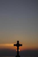 The silhouette of a cross on the background of a twilight sunset is a symbol of God and the cross is also believed to be of His divinity. The cross is a symbol of God loving kindness for all people. photo