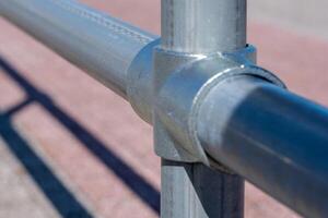 Shadow of metal pipes connected by fasteners on light pink pavement on sunny day photo