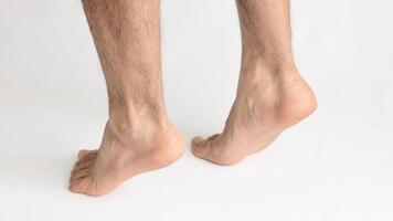 Two male feet standing on tiptoe showing tension in the Achilles tendon, with white background photo