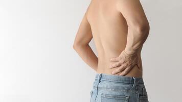 Shirtless man turning his back and touching his lower back with his hand due to pain, white background with space for text on the left photo