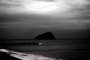 dark sea waves crash on the sandy coast of the Ligurian coast in a dark and noir setting photo