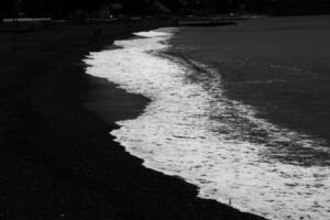 dark sea waves crash on the sandy coast of the Ligurian coast in a dark and noir setting photo