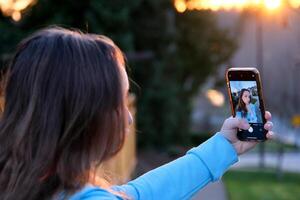 interesado atractivo mujer en marrón atuendo haciendo autofoto magnífico niña tomando imagen de sí misma mientras caminando alrededor ciudad. foto