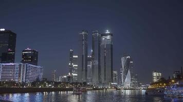 Evening city. Action. Huge tall evening buildings located next to the river and everything is lit with lanterns. video