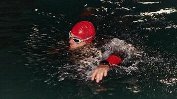 un determinado profesional triatleta sufre riguroso noche hora formación en frío aguas, exhibiendo Dedicación y Resiliencia en preparación para un próximo triatlón nadar competencia foto