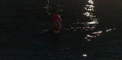 A determined professional triathlete undergoes rigorous night time training in cold waters, showcasing dedication and resilience in preparation for an upcoming triathlon swim competition photo