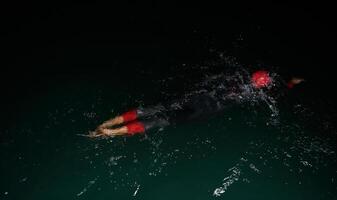 A determined professional triathlete undergoes rigorous night time training in cold waters, showcasing dedication and resilience in preparation for an upcoming triathlon swim competition photo