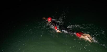 A determined professional triathlete undergoes rigorous night time training in cold waters, showcasing dedication and resilience in preparation for an upcoming triathlon swim competition photo