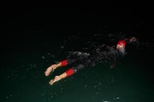 A determined professional triathlete undergoes rigorous night time training in cold waters, showcasing dedication and resilience in preparation for an upcoming triathlon swim competition photo