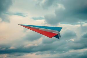Dynamic shot of a red, white, and blue paper airplane flying against a cloudy sky photo