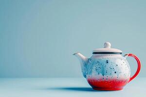 A quirky teapot painted in red, white, and blue, on a blue to white gradient background photo