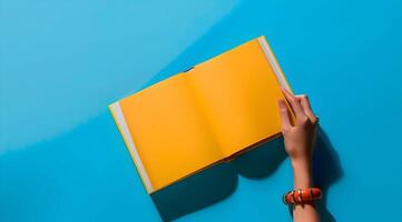 libro burlarse de arriba con un mano aislado en un azul antecedentes. un mano participación un abierto amarillo revista con amarillo vacío página. foto