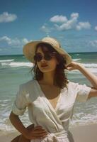 mujer en pie en playa con sombrero y Gafas de sol foto