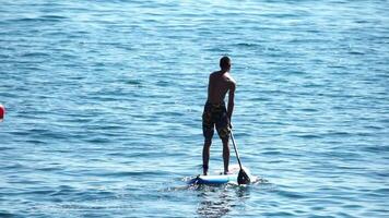 homem sup mar. Forte Atlético homem aprende para remo sup em pé em borda dentro aberto mar oceano em ensolarado dia. verão feriado período de férias e viagem conceito. aéreo visualizar. lento movimento video