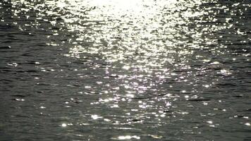 Abstract shining sun reflections on blue surface of sea waves. Bokeh sun glare reflected in water surface. The shimmering small sea waves in sun. Sea on sunny day. Natural bokeh texture. Slow motion video