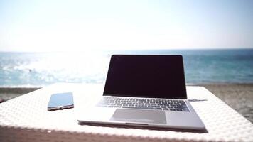 moderno taccuino e smartphone a mare oceano spiaggia bar piace Perfetto posto di lavoro per distanza libero professionista. il computer portatile computer con finto su vuoto schermo per pubblicizzare contenuto. lento movimento video