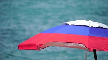 white blue red colored beach umbrellas or parasols against blue sea during a sunny day on a beach. Symbol of vacations, relax, summer. Colorful umbrellas from the sun stand on the beach. Slow motion. video