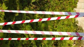 Red and white warning tape swinging in the wind. Protection sign. Don't cross the line. Red White caution tape pole fencing is protects for No entry. Green blured backdrop without people, empty street video
