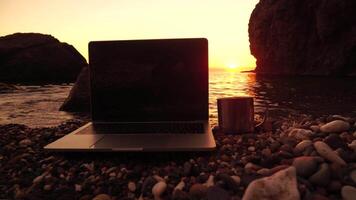Silhouette of laptop and cup on the beach over sea sunset. Sparkling sea water on background. Freelancer, blogger working on notebook on the beach. video