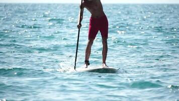 Man Sup Sea. Strong athletic man learns to paddle sup standing on board in open sea ocean on sunny day. Summer holiday vacation and travel concept. Aerial view. Slow motion video