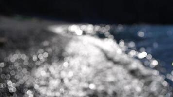 Abstract sea summer ocean sunset nature bokeh background. Small waves on azure water surface in motion blur with golden bokeh lights from sun. Holiday, vacation and recreational concept. Slow motion video