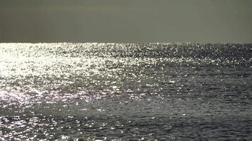 Abstract shining sun reflections on blue surface of sea waves. Bokeh sun glare reflected in water surface. The shimmering small sea waves in sun. Sea on sunny day. Natural bokeh texture. Slow motion video