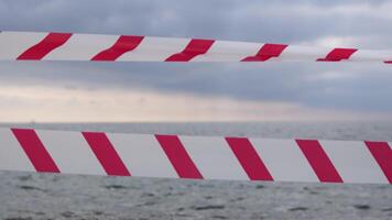 rojo blanco advertencia cinta barrera cinta balanceo en el viento a través de exótico mar playa antecedentes sin gente. No entrada rojo blanco precaución cinta. No fiesta concepto, retrasado viajar, No verano planes video