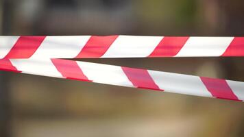 Red and white warning tape swinging in the wind. Protection sign. Don't cross the line. Red White caution tape pole fencing is protects for No entry. Backdrop without people, empty street. Close up video