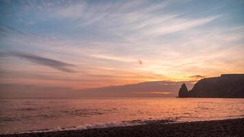 Sunset Sky Clouds Timelapse. A red burning sunset over the sea rocky volcanic cliff. Abstract nature summer ocean sea background. Small waves on golden warm water surface with bokeh lights from sun. video