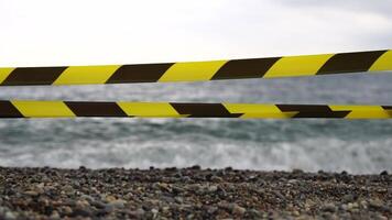 Yellow black warning tape barrier ribbon swinging in the wind across exotic sea beach background without people. No entry Yellow black caution tape. No holiday concept, delayed travel, no summer plans video