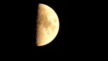 A glowing golden huge half moon seen from earth through the atmosphere against a starry night sky. A large moon moves across the sky, the moon moving from the left frame to the right. video