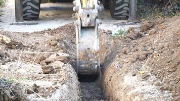 Excavator digs a trench to lay pipes. Close up of an excavator digging a deep trench. An excavator digs a trench in the countryside to lay a water pipe. Slow motion video